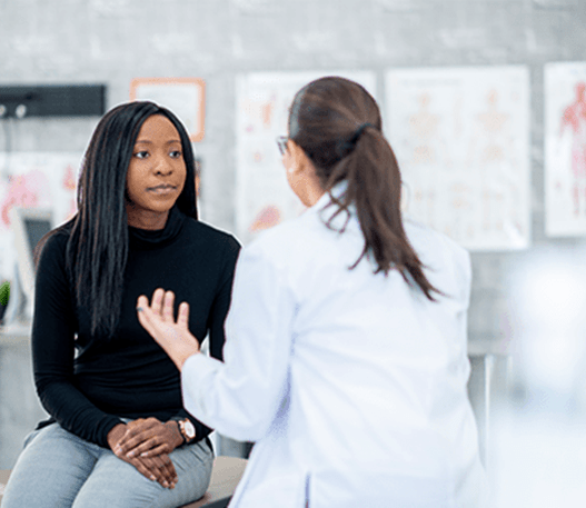 A young woman sitting on an examination table, talking to her doctor